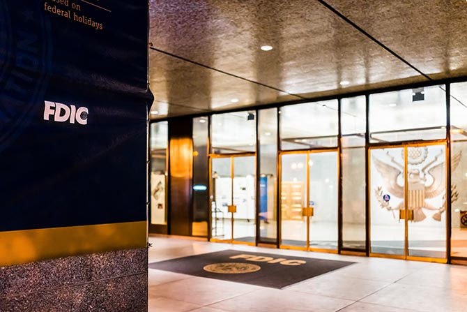 FDIC Interest Rate Restrictions; FDIC office entrance with reflective glass doors and a large emblem on the floor. The FDIC logo is visible on a wall, conveying formality and security.